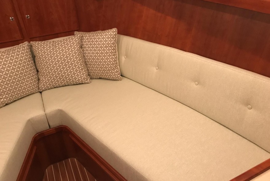 Beige L-shaped sofa with three patterned cushions in a wood-paneled boat cabin interior.