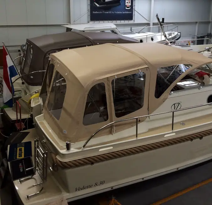 White motor yacht with a beige canopy on display in a showroom, model Vedette 8.30 visible at the stern.