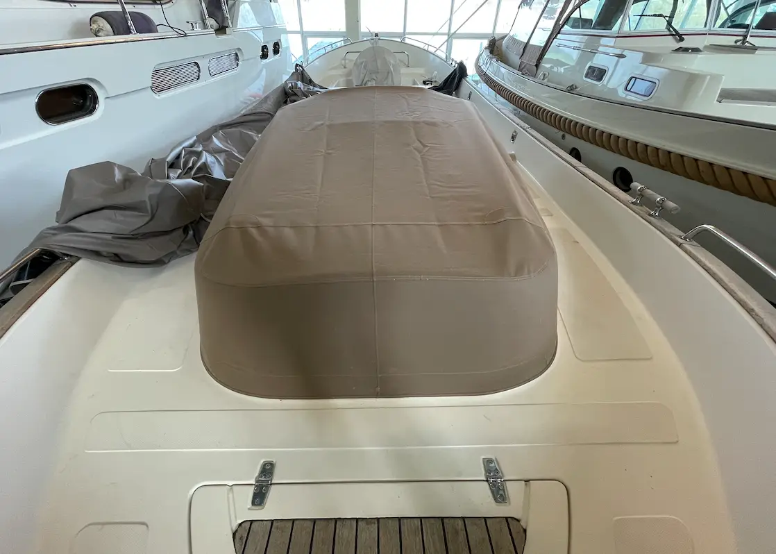 A white luxury boat indoors with a large brown canvas cover over the cockpit area, flanked by other yachts in a showroom or marina.