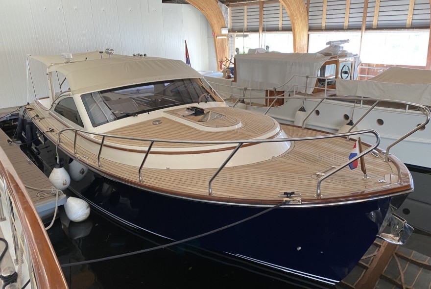 Luxury motor yacht docked in an indoor marina, featuring a teak deck, white superstructure, and navy hull.