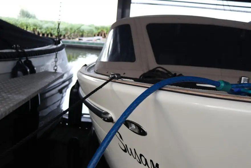 Close-up of a white motorboat tied to a dock with blue and black mooring lines and a metal cleat visible on its bow.