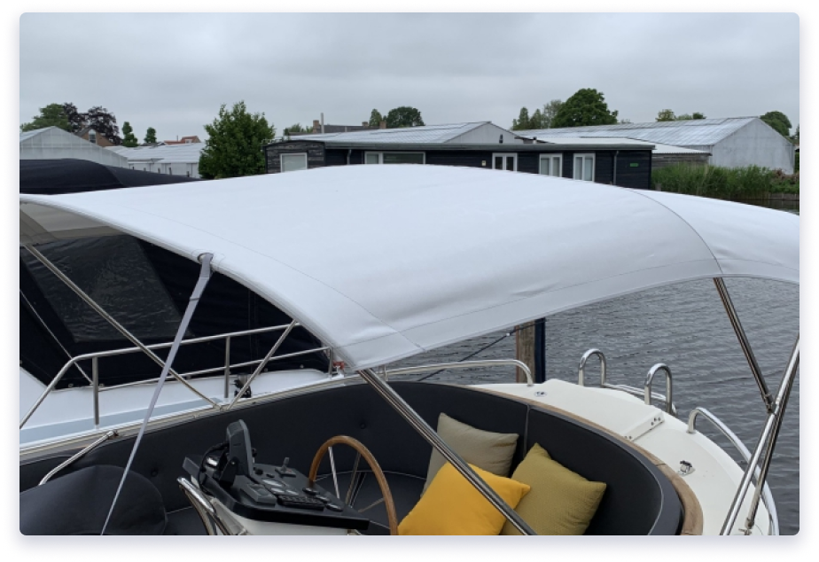 White canopy over a boat's cockpit with a steering wheel and yellow cushions on a docked vessel by the water.