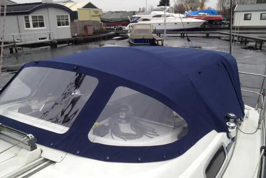 Blue canvas boat cockpit cover over a white sailboat at a marina with other boats and docks in the background