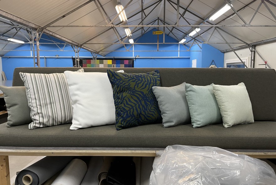 Grey sofa with striped, white, and blue cushions on a showroom platform; blue wall and exposed roof trusses behind the scene.