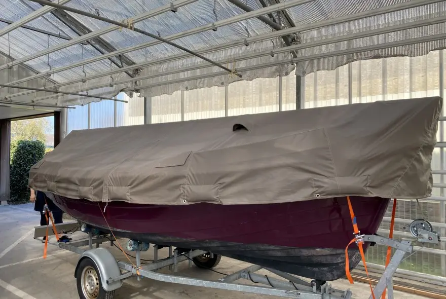 Boat on a trailer, fully covered with a beige canvas boat cover in a covered storage area.