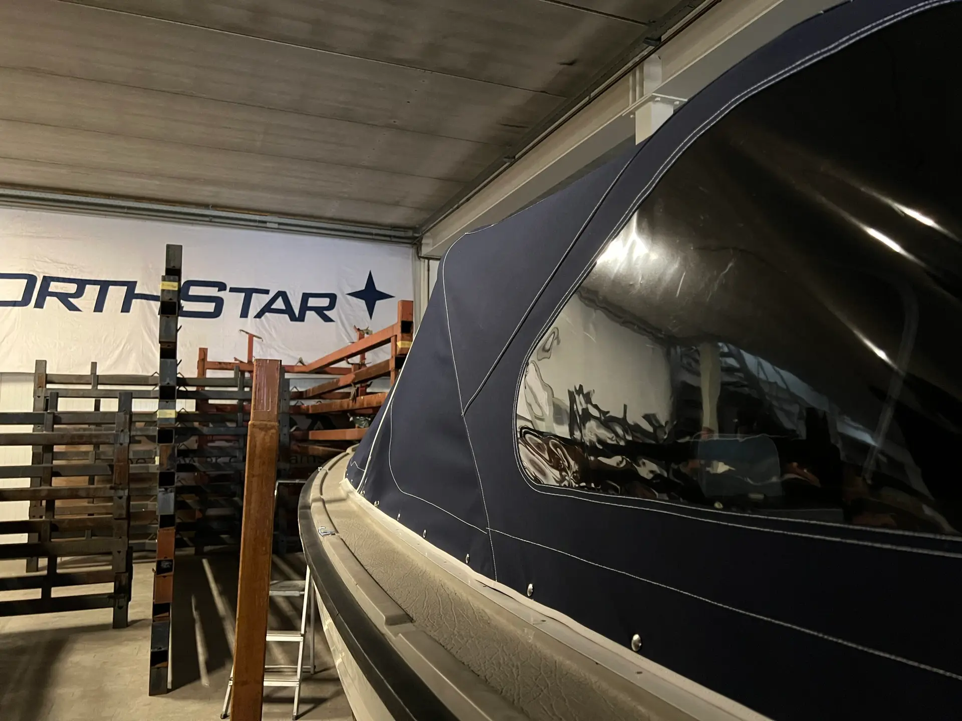 A large navy boat inside a warehouse, with metal scaffolding and a 'NORTH STAR' banner in the background.