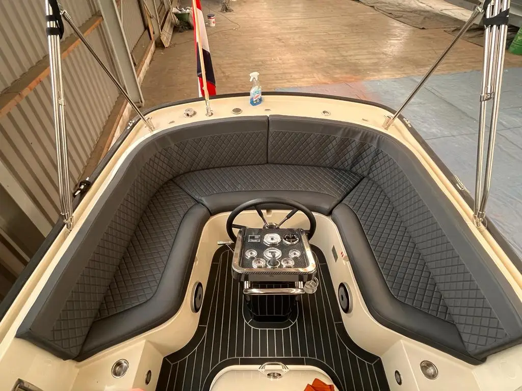 Boat cockpit with U-shaped cushioned seating, central steering wheel, and gauge panel in a workshop setting.