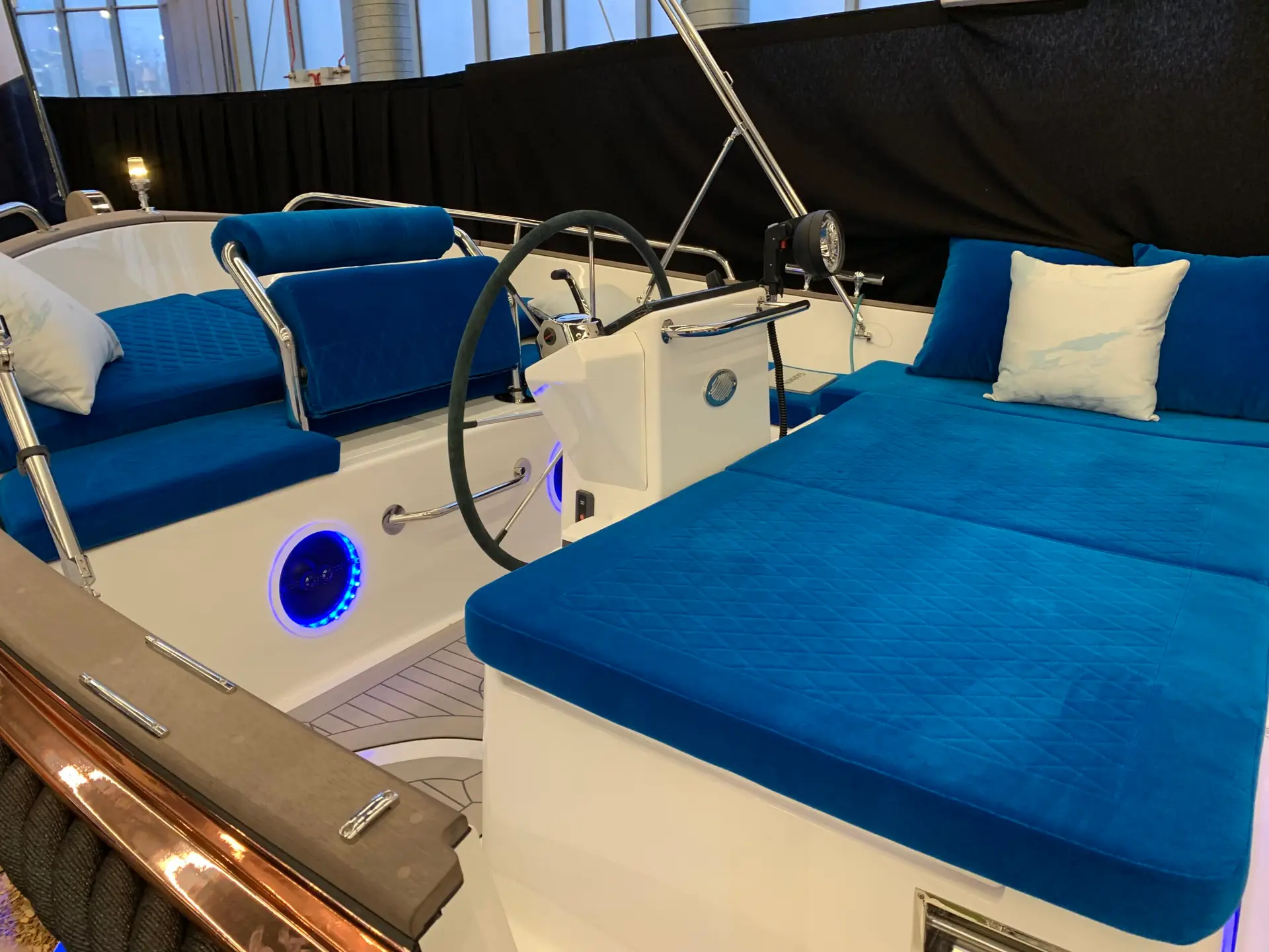 Boat cockpit interior with bright blue cushioned seats and white fiberglass, steering wheel center, and blue LED lighting accents.