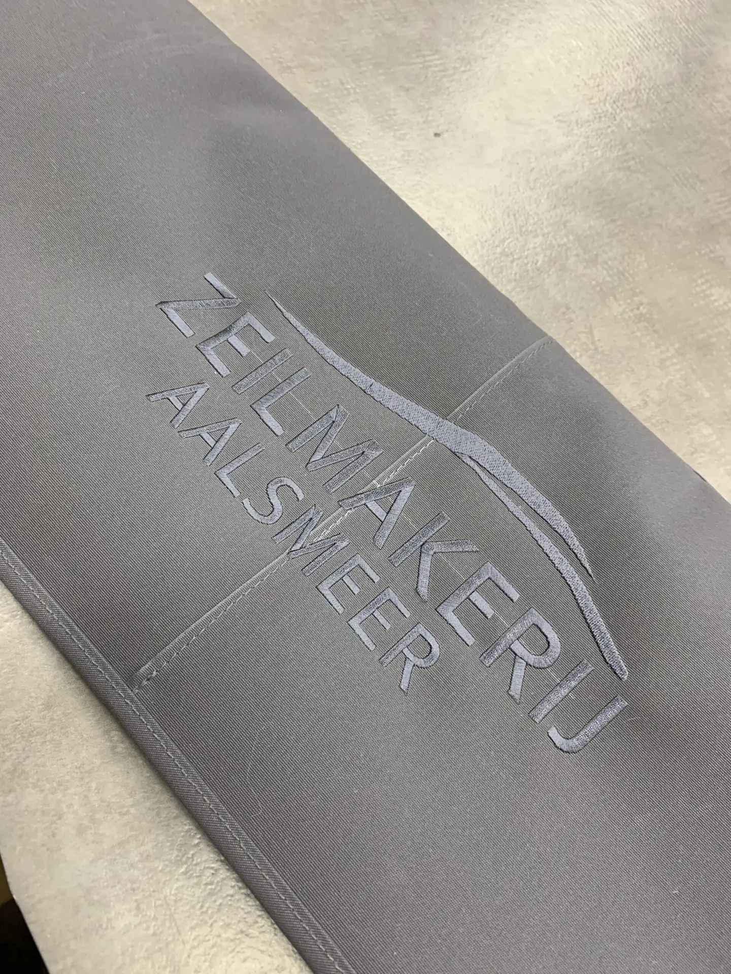 Close-up of gray fabric with light gray embroidered text reading 'FEMME' along a seam.