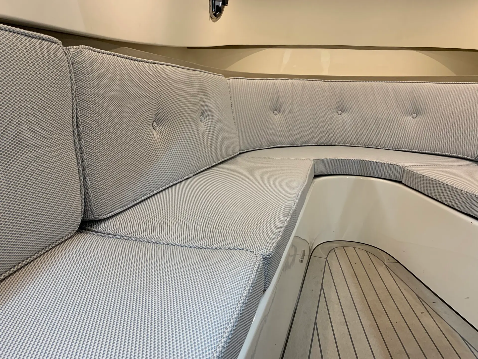 Gray curved sectional seating in a boat cabin with tufted buttons and a wooden deck nearby